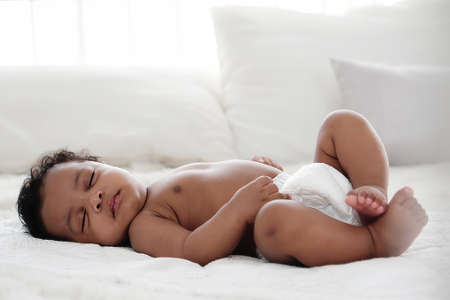 portrait of african american baby girl sleeping on white bed