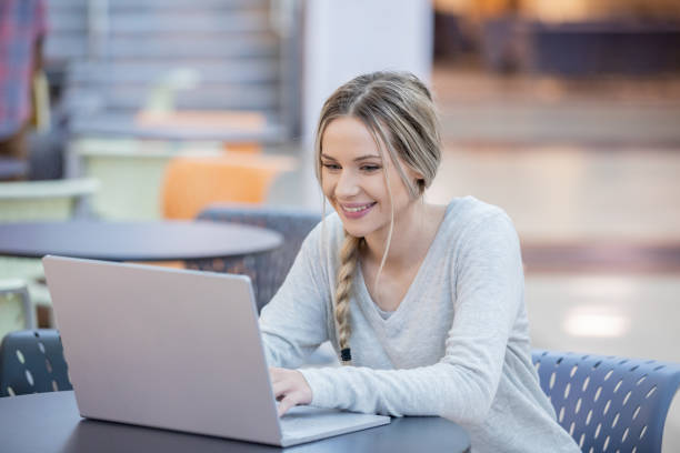 istock Young adult student smiling and typing notes on laptop while studying in college building 1198534586