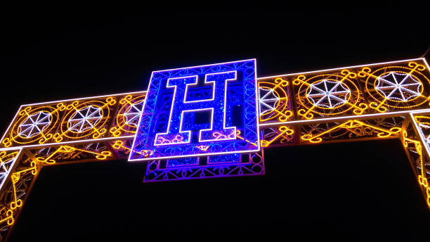 The upper part of a rectangular yellow-white led light arch with a blue letter H in the middle. Outdoor holiday decoration led light in street at night.