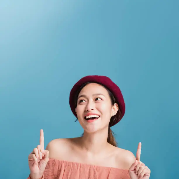 Photo of Portrait of confident beautiful asian woman with hand pointing up and looking up isolated on blue color background with studio shot.Skincare for healthy face concept.
