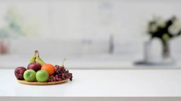 Photo of Close up view of fruit tray and copy space on marble desk with blurred kitchen room