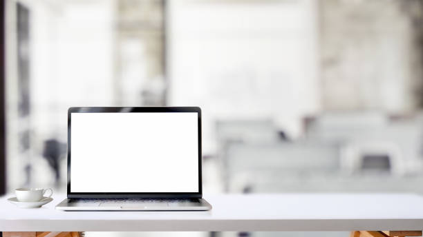 istock Cropped shot of simple workspace with blank screen laptop and coffee cup on white table with blurred office room 1198552589