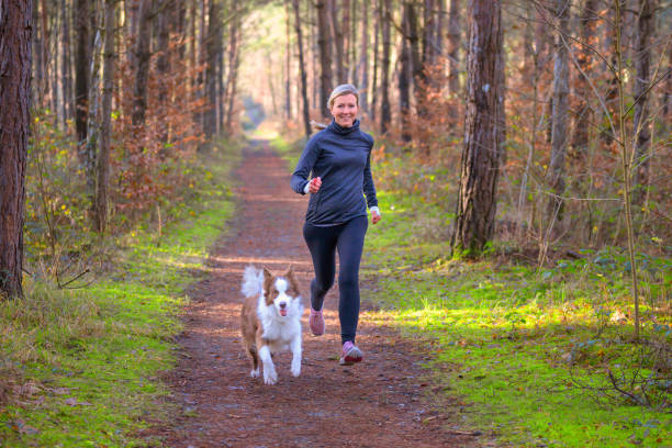 Healthy fit woman running with her dog Healthy fit woman running with her dog jogging together through a forest along a footpath approaching the camera with a happy smile individual sports stock pictures, royalty-free photos & images
