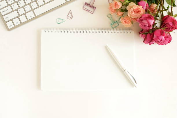istock flat lay top view women's office desk on  white background selective focus. Female workspace with laptop, beautiful pink roses flowers in a vase, gift box, accessories, notebook mock up, glasses. 1198560613