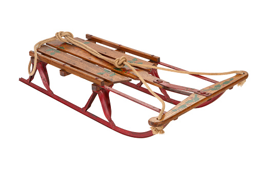 Antique Wooden Sled with red metal running blades. There is a rope attached for steering.  This sled is an antique and it was probably used during the 1940s. The image is shown at an angle, and is in full focus from front to back. The image is isolated on a white background, and includes a clipping path.