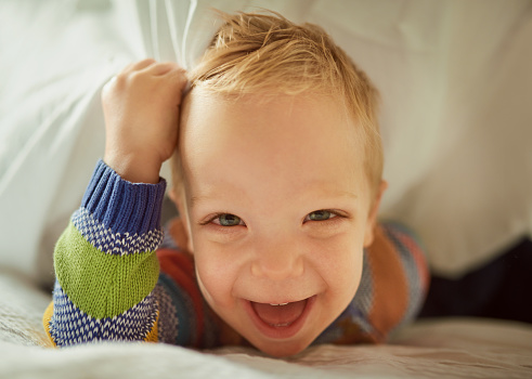 Shot of an adorable little boy playing under the duvet at home