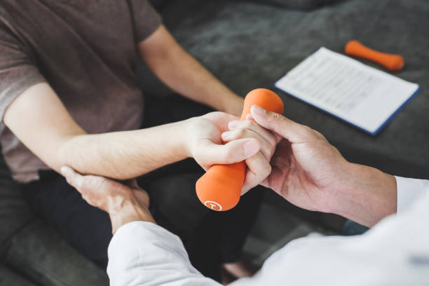 uomo fisioterapista che dà esercizio fisico con trattamento del manubrio circa braccio e spalla del paziente maschio atleta terapia fisica visita la casa del paziente - human muscle human arm bicep muscular build foto e immagini stock