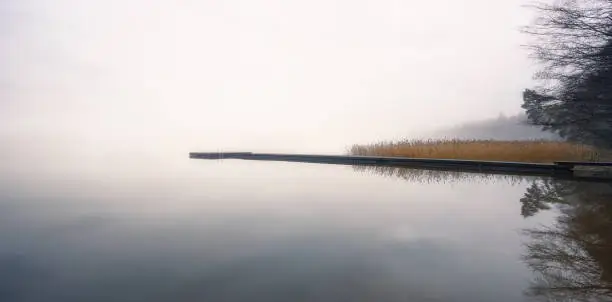 Photo of Foggy landscape with calm lake and wooden pier at tranquil autumn morning in Finland
