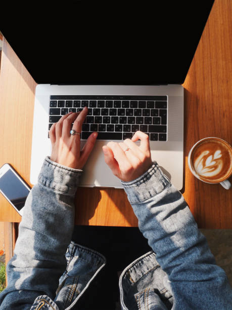 pemandangan atas tangan gadis yang bekerja pada laptop minum kopi di ruang kerja bersama yang cerah - contributor potret stok, foto, & gambar bebas royalti