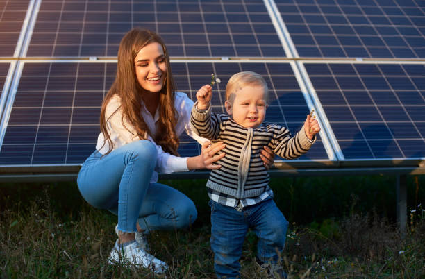 Mother with her little son by solar panels Young mother supporting her little son in making his first steps near solar panels, concept of modern family baby squatting stock pictures, royalty-free photos & images