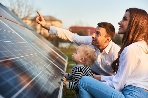 Hombre muestra a su familia los paneles solares en la parcela cerca de la casa durante un día cálido photo
