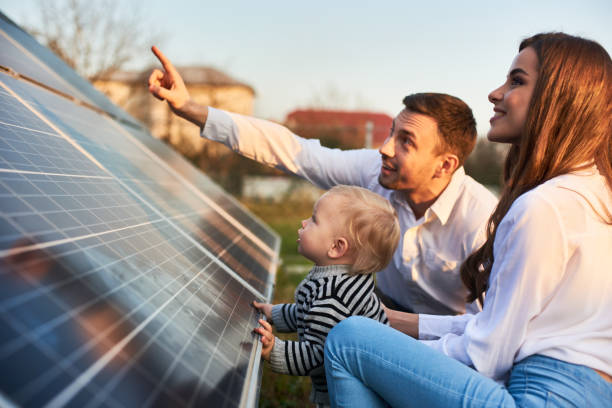 l'uomo mostra alla sua famiglia i pannelli solari sulla trama vicino alla casa durante una giornata calda - pannelli solari foto e immagini stock