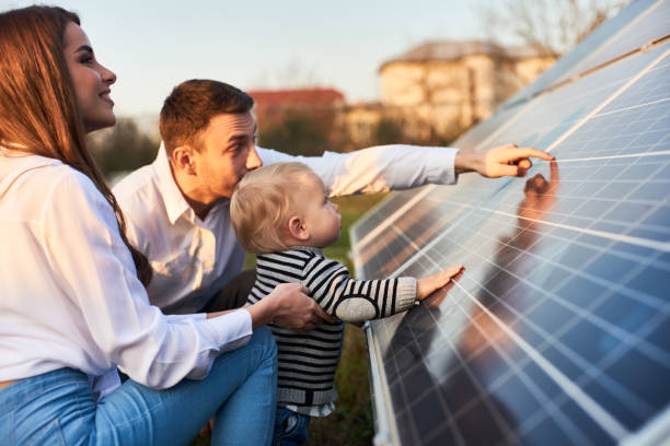 Young family getting to know alternative energy Side close-up shot of a young modern family with a little son getting acquainted with solar panel on a sunny day, green alternative energy concept rooftop solar stock pictures, royalty-free photos & images