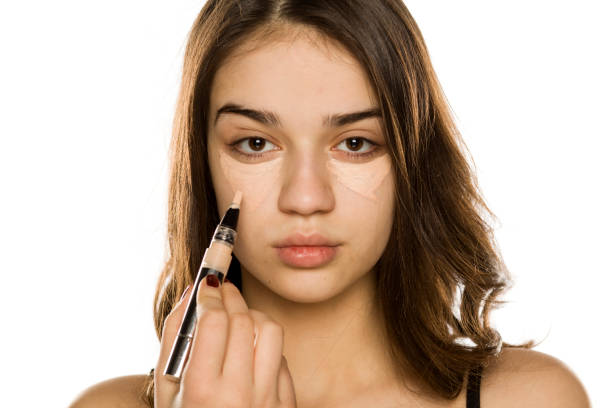 istock Young beautiful woman applying concealer on white background 1198585516