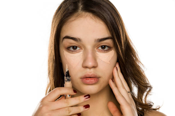 istock Young beautiful woman applying concealer on white background 1198585518