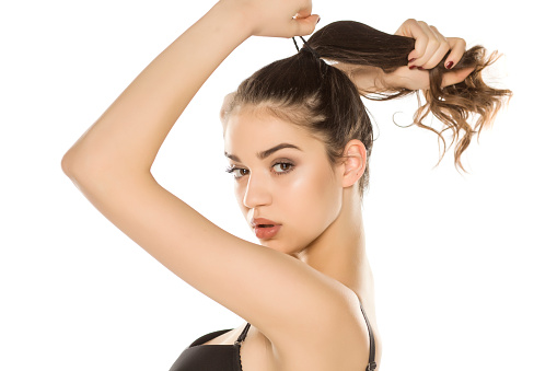 Young woman with makeup  tying her hair on white background