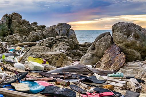 Dozens of old plastic flip flops and shoes are washed up or discarded on the beach.  They represent the massive environmental issue that is Global Ocean Pollution.  They have possibly been dumped, a crime known as Fly-tipping.  Location is Ko Lanta, Krabi province, Thailand.