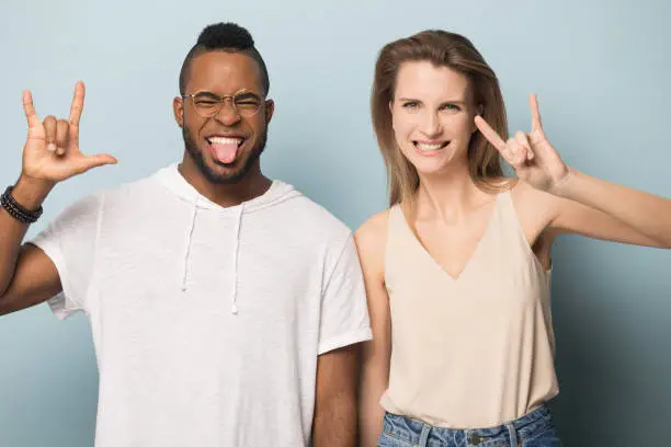 Photo of Excited multiethnic man and woman show rock-n-roll hand gesture