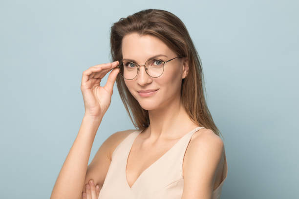 Portrait of millennial woman posing in glasses in studio Headshot portrait of beautiful Caucasian woman isolated on blue studio background wear glasses look at camera, millennial female in spectacles posing advertising optician, sight correction treatment beautiful women giving head stock pictures, royalty-free photos & images