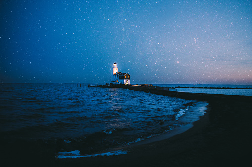 View of bright starry sky, white lighthouse and Northern sea in Netherlands during wintertime