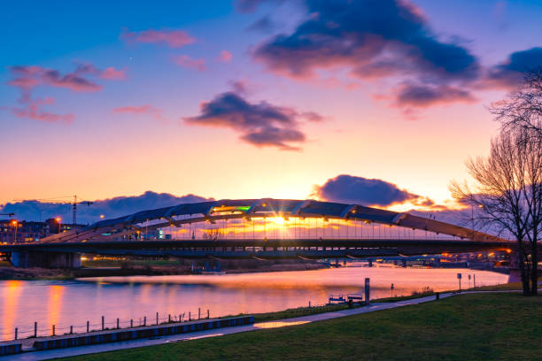 puente colgante kotlarski sobre el río vístula en cracovia, polonia, contra la luz de la puesta de sol púrpura y naranja con la reflelection de agua. destello de lente solar excepcional. - photography suspension bridge water night fotografías e imágenes de stock