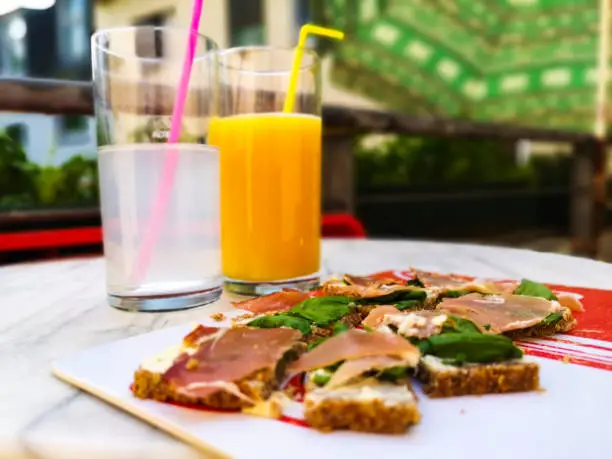 Ham on bread with butter and basil on the balkony with two glases of juice on a table