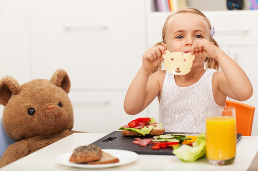 Little girl making a sandwich to her toy bear - having a healthy snack with it sitting at a small table
