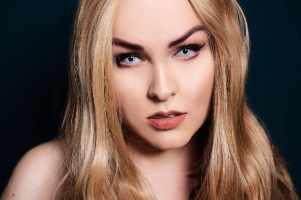 istock Blonde with long hair looking at the camera. Professional makeup, beautiful eyebrows, white lenses. Looking vampires, bright eyes. Hair care. Blindinka on a black back 1198605829