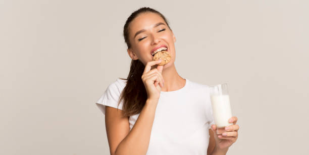 menina que aprecia o leite e os bolinhos que estão sobre o fundo cinzento, panorama - cookie women eating beautiful - fotografias e filmes do acervo