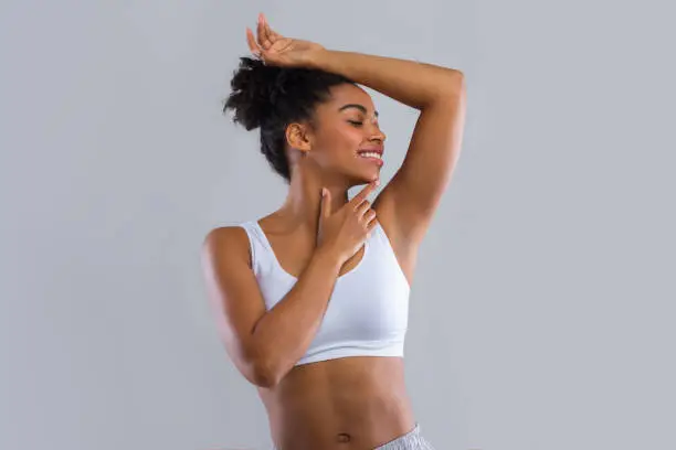 Photo of Happy afro girl smelling her armpit over grey background