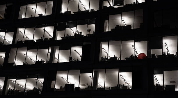 istock Office building exterior at night with interior lights on. Empty offices with red umbrella behind the window. 1198606894