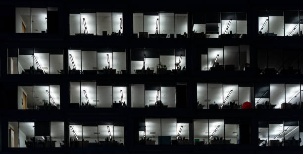 istock Office building exterior at night with interior lights on. Empty offices with red umbrella behind the window. 1198606895