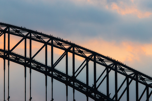 Silhouette of people walking on top of the Sydney Harbour Bridge.