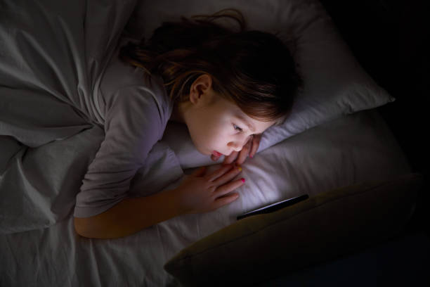 istock little girl on bed watching mobile phone at night 1198614096
