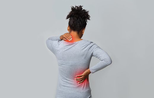 Back view of african woman rubbing her inflamed neck and loins, grey background