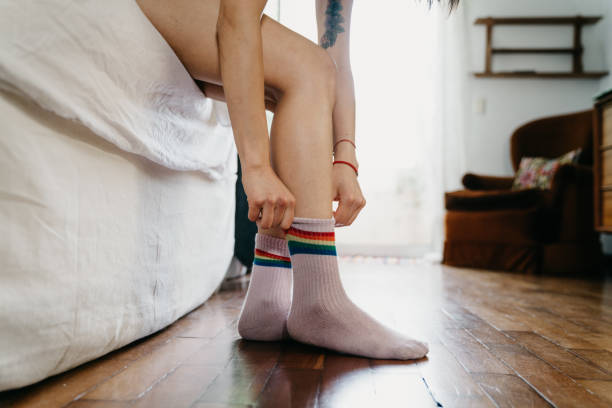 Young adult woman waking up, putting on rainbow flag socks Young adult woman waking up, putting on rainbow flag socks. Selective focus on the feet. woman putting on socks stock pictures, royalty-free photos & images