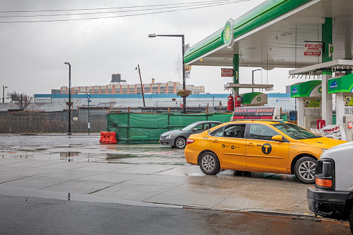 21st Street, Queens, New York, USA, December 2, 2019: Yellow cab at a gas station with a view to traditional water tanks on a roof, Christmas decoration and on a rainy day