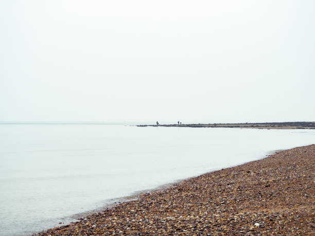 View of Kent Coastline with white cloudy sky Pebbled beach on the Kent coast near Reculver Towers on cloudy New Year's day, with incidental people herne bay photos stock pictures, royalty-free photos & images