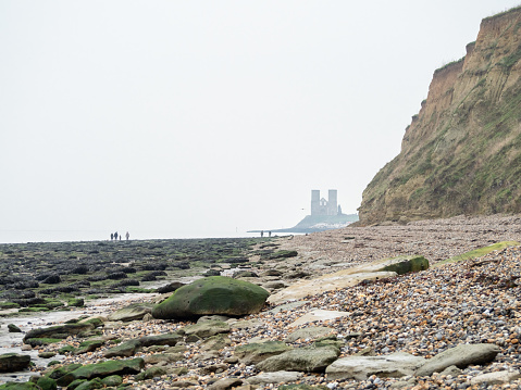 Pebbled beach on the Kent coast near Reculver Towers on cloudy New Year's day, with the Roman fort in the distance