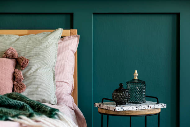 istock Modern bedroom interior with design coffee table, glassy boxes and elegant personal accessories. Beautiful bed sheets, blanket and pillows. Template. Stylish home staging. Wall panelling. Details 1198618836