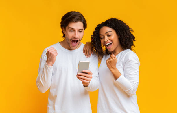 Happy interracial couple looking at smartphone screen and celebrating success