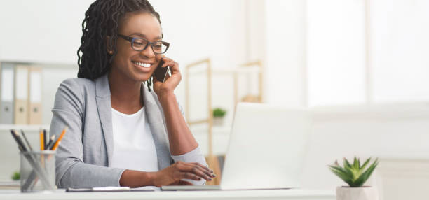 Black Businesswoman Talking On Cellphone And Using Laptop In Office, Panorama Lady Boss. Afro Businesswoman Talking On Cellphone While Working On Laptop In Modern Office, Wide Horizontal Banner, Panorama With Free Space language photos stock pictures, royalty-free photos & images
