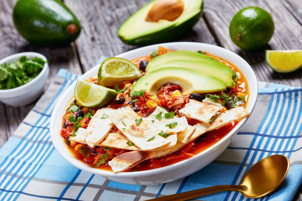 istock Chicken Taco Soup with black bean, corn kernels, topped with tortilla strips, avocado slices and lime 1198620784