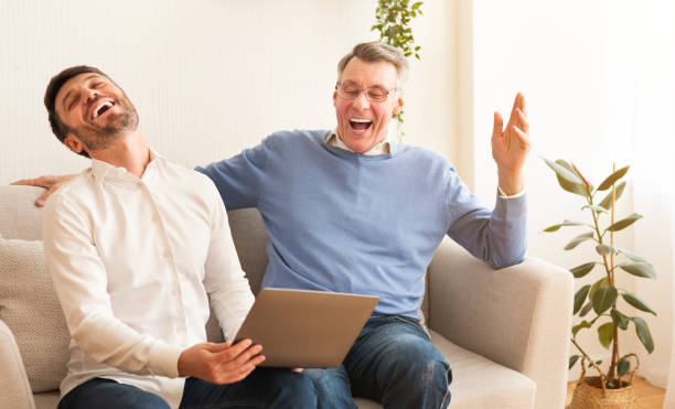 istock Senior Man And Son Using Laptop Laughing Sitting On Sofa 1198620785