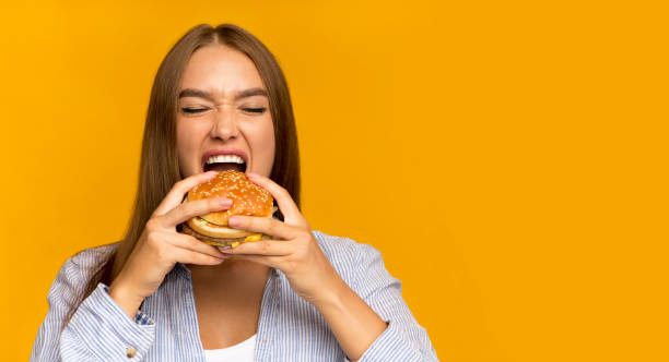 istock Young Lady Biting Burger Enjoying Junk Food, Panorama, Studio Shot 1198621347