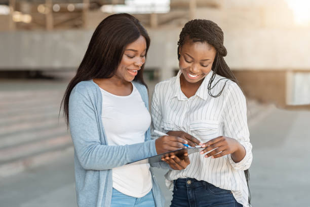 Afro female interviewing young woman on street for social research Survey. Black female interviewing young girl for social research, asking her questions on street and taking notes petition stock pictures, royalty-free photos & images