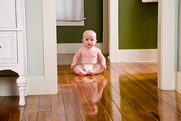 Wondered infant in a denim dress sits on a floor at home