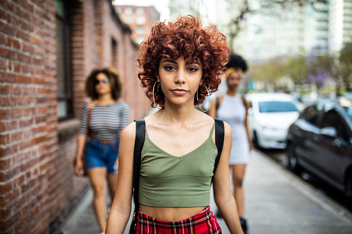 Latin woman walking down the street with her best friends, two women walking behind her
