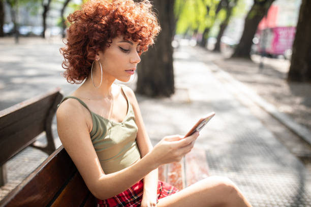 istock Latin Girl sitting on bench and text messaging on phone 1198622461