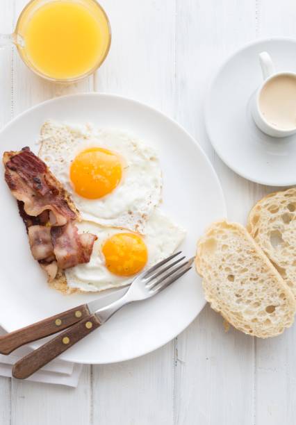 istock Full American Breakfast on white, top view, copy space. Sunny side fried eggs, roasted bacon, hash brown,  orange juice and coffee for breakfast. 1198623348